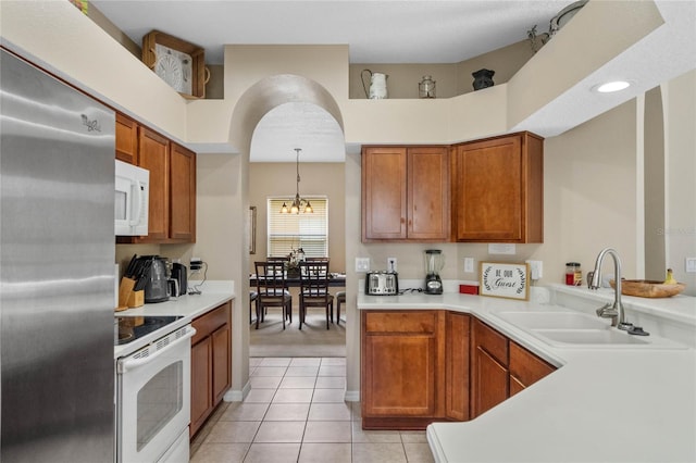 kitchen with light countertops, light tile patterned floors, brown cabinetry, white appliances, and a sink