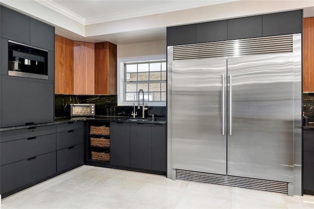 kitchen featuring a sink, dark stone counters, ornamental molding, and stainless steel built in refrigerator