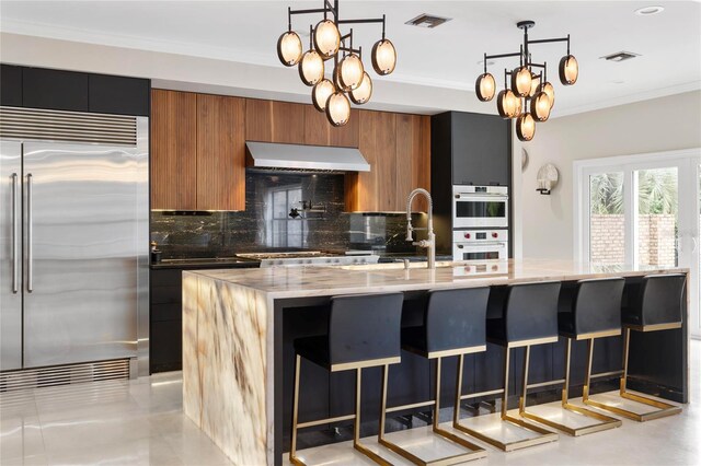 kitchen with visible vents, wall chimney range hood, brown cabinets, stainless steel appliances, and modern cabinets