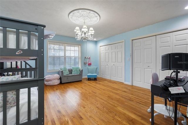 bedroom with a notable chandelier, wood finished floors, baseboards, and two closets