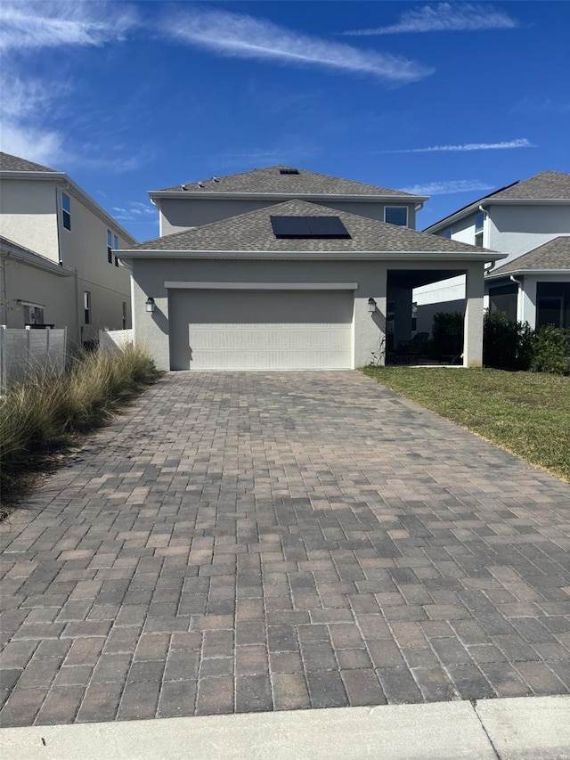 view of front of house featuring solar panels, a shingled roof, stucco siding, decorative driveway, and a garage