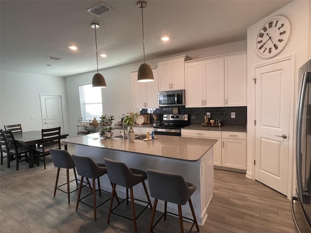 kitchen featuring visible vents, a breakfast bar, white cabinets, appliances with stainless steel finishes, and tasteful backsplash