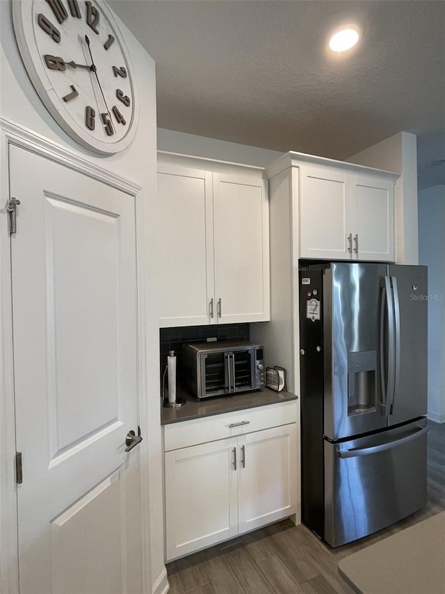 kitchen with stainless steel refrigerator with ice dispenser, dark countertops, white cabinets, a toaster, and dark wood-style flooring