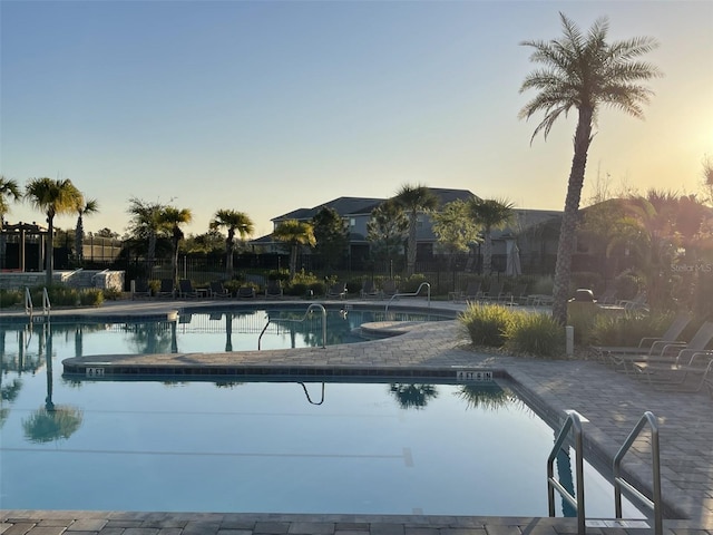 pool at dusk with a patio, a community pool, and fence