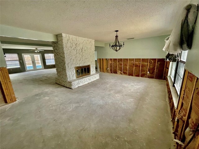 unfurnished living room with visible vents, unfinished concrete flooring, a textured ceiling, a stone fireplace, and a chandelier