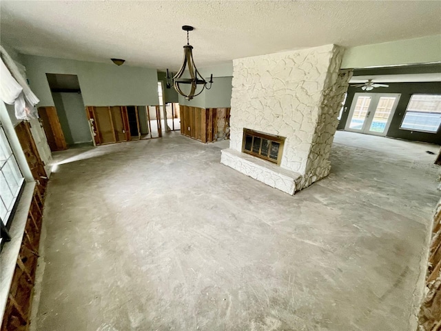 unfurnished living room with unfinished concrete floors, a chandelier, a textured ceiling, and a stone fireplace