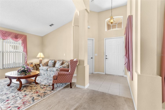 foyer entrance with light tile patterned floors, high vaulted ceiling, a textured ceiling, light carpet, and visible vents