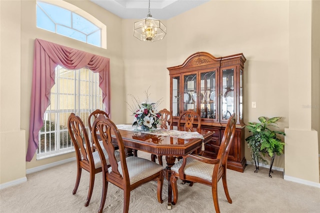 dining area featuring light carpet, baseboards, a towering ceiling, and a chandelier