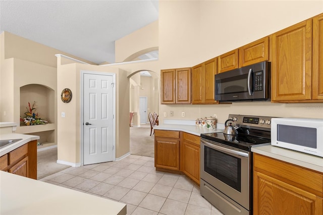 kitchen with brown cabinetry, white microwave, stainless steel electric stove, light countertops, and light tile patterned flooring