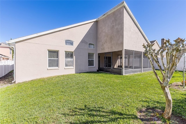 rear view of house featuring stucco siding, fence, a sunroom, and a yard