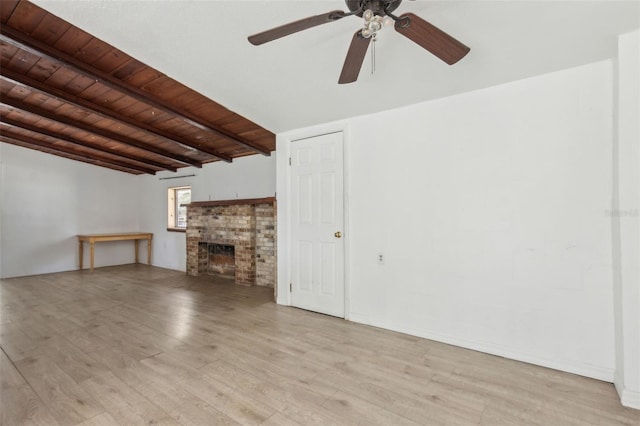 unfurnished living room with beam ceiling, ceiling fan, wood ceiling, a brick fireplace, and light wood-type flooring