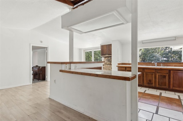 kitchen featuring baseboards, lofted ceiling, light wood-style flooring, a sink, and tile counters