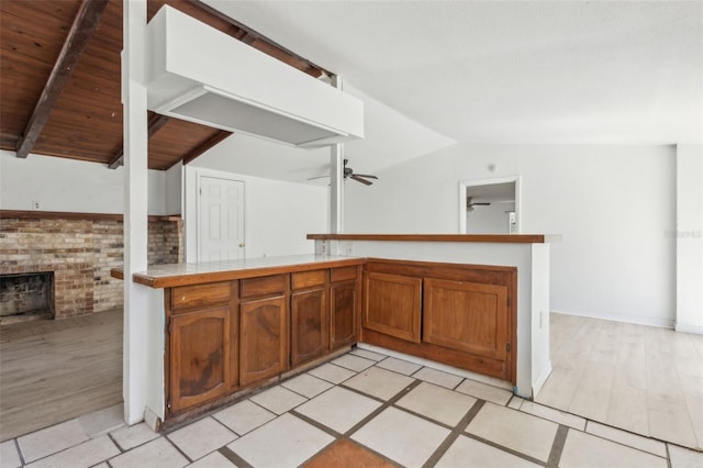 kitchen featuring lofted ceiling, a brick fireplace, a ceiling fan, and brown cabinets