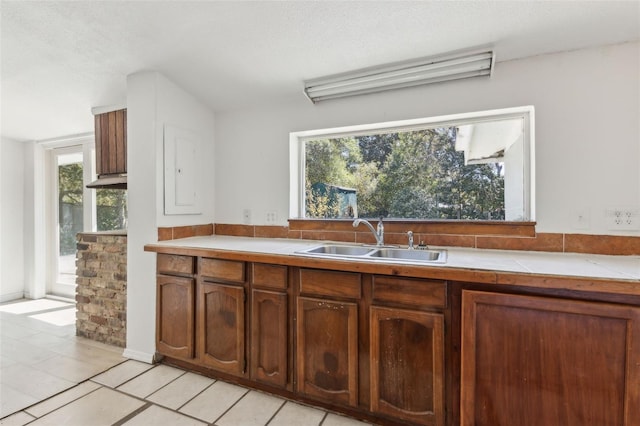 kitchen featuring light tile patterned floors, tile countertops, brown cabinets, and a sink