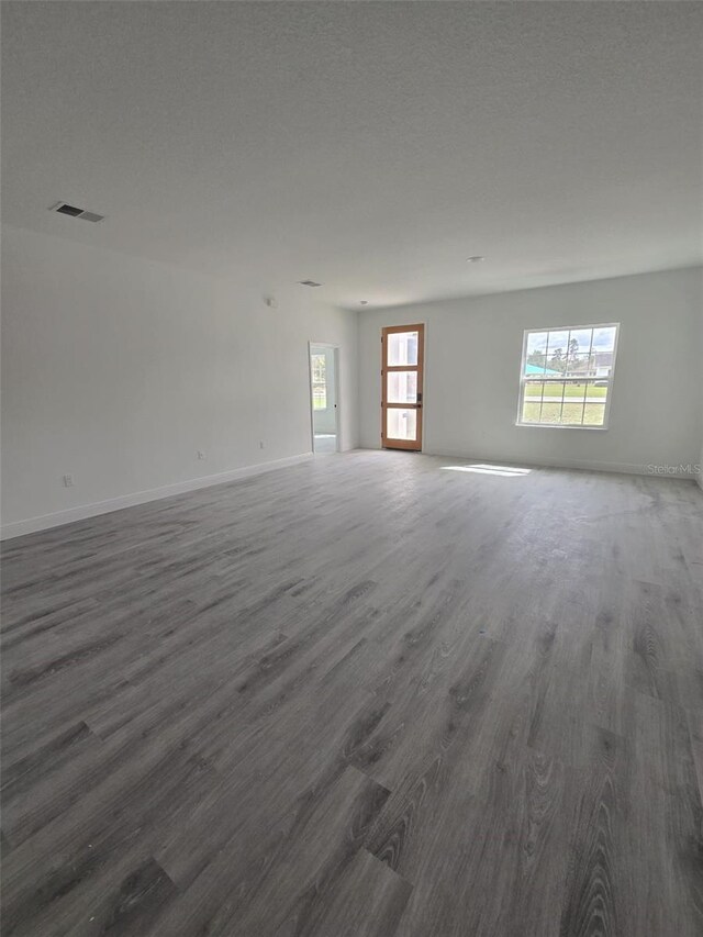 empty room featuring a textured ceiling, dark wood-type flooring, visible vents, and baseboards