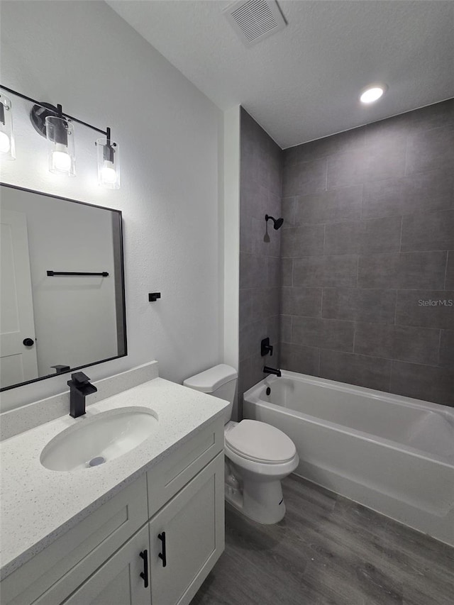 bathroom featuring shower / bath combination, visible vents, toilet, wood finished floors, and vanity
