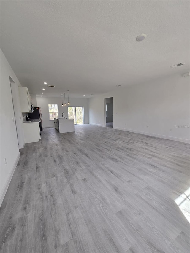 unfurnished living room featuring a sink, light wood-style floors, baseboards, and a textured ceiling