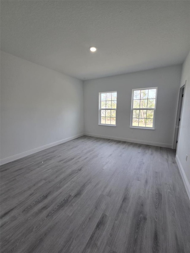 unfurnished room featuring a textured ceiling, dark wood-style flooring, and baseboards