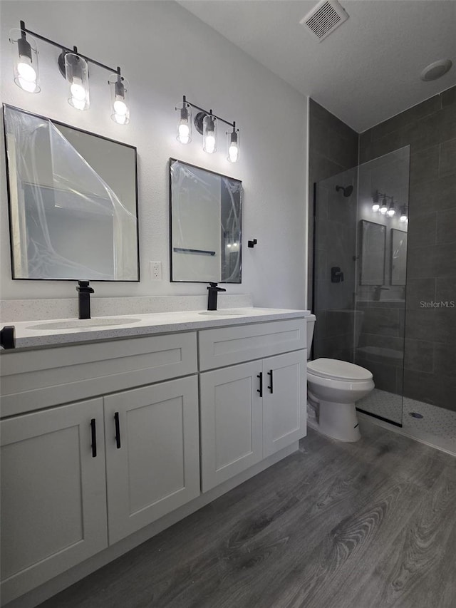 full bath featuring a tile shower, wood finished floors, a sink, and visible vents