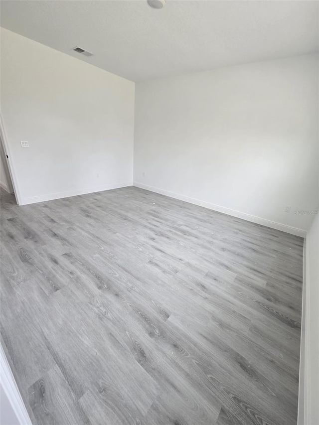spare room featuring baseboards, visible vents, and wood finished floors