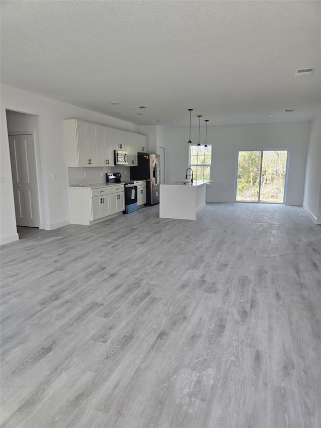unfurnished living room featuring a textured ceiling, a sink, visible vents, and light wood-style floors