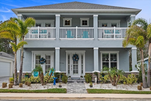 view of front facade featuring covered porch, roof with shingles, a balcony, and stucco siding