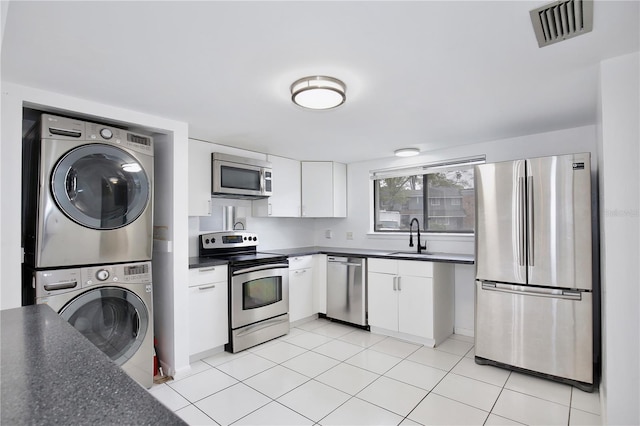 kitchen with visible vents, dark countertops, stacked washer / drying machine, stainless steel appliances, and a sink