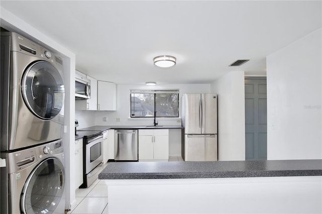 kitchen with stainless steel appliances, dark countertops, visible vents, white cabinets, and stacked washing maching and dryer