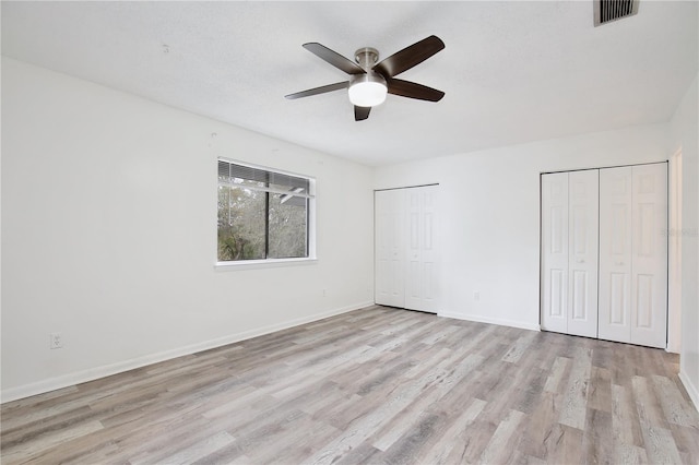 unfurnished bedroom featuring light wood finished floors, baseboards, visible vents, and multiple closets