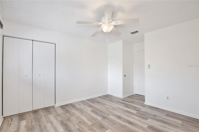 unfurnished bedroom with a textured ceiling, visible vents, baseboards, a closet, and light wood finished floors