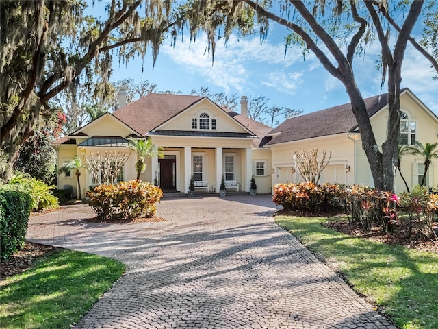 greek revival inspired property featuring decorative driveway, a chimney, stucco siding, a standing seam roof, and metal roof