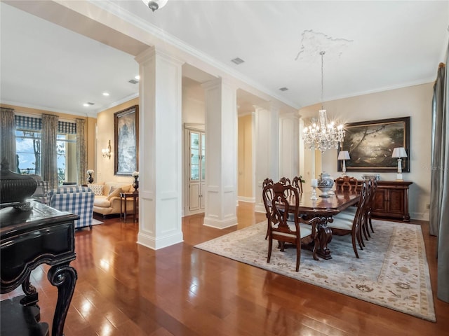 dining room featuring a notable chandelier, wood finished floors, visible vents, ornamental molding, and ornate columns