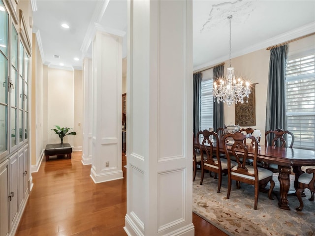 dining area featuring wood finished floors, an inviting chandelier, crown molding, ornate columns, and recessed lighting