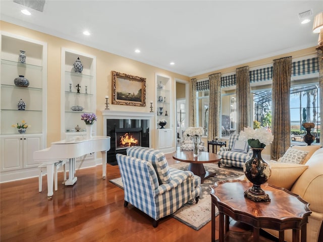 living area with a warm lit fireplace, built in shelves, visible vents, and wood finished floors