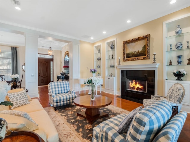 living area with built in shelves, crown molding, recessed lighting, wood finished floors, and a tile fireplace