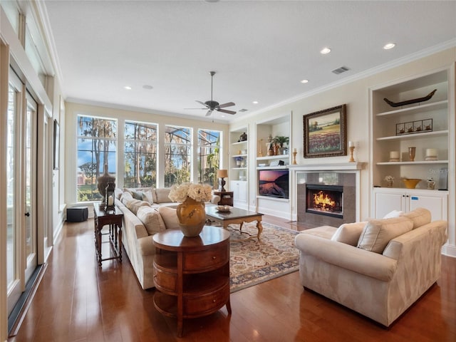 living room featuring built in shelves, dark wood-style floors, crown molding, a fireplace, and visible vents