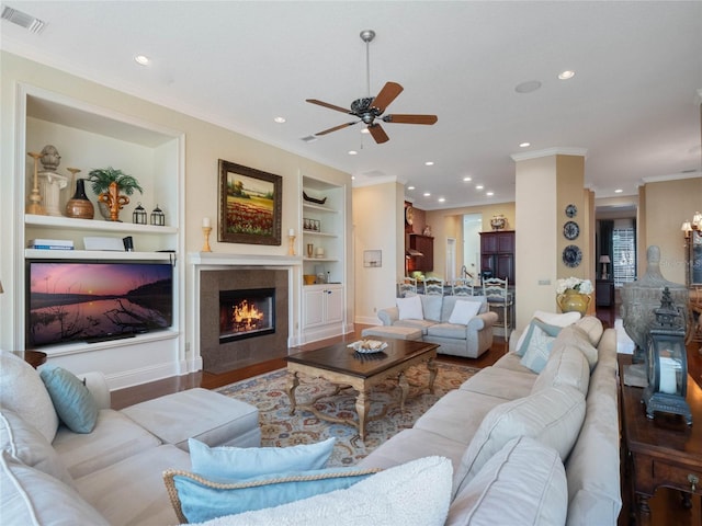 living area with built in shelves, crown molding, visible vents, a tiled fireplace, and wood finished floors