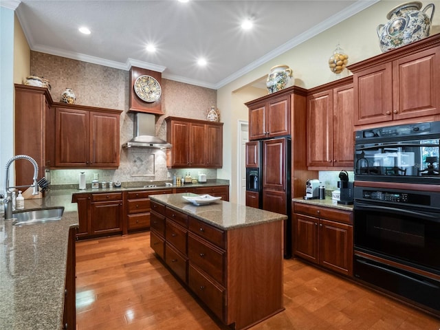 kitchen featuring light wood finished floors, a kitchen island, a sink, wall chimney range hood, and dark stone counters