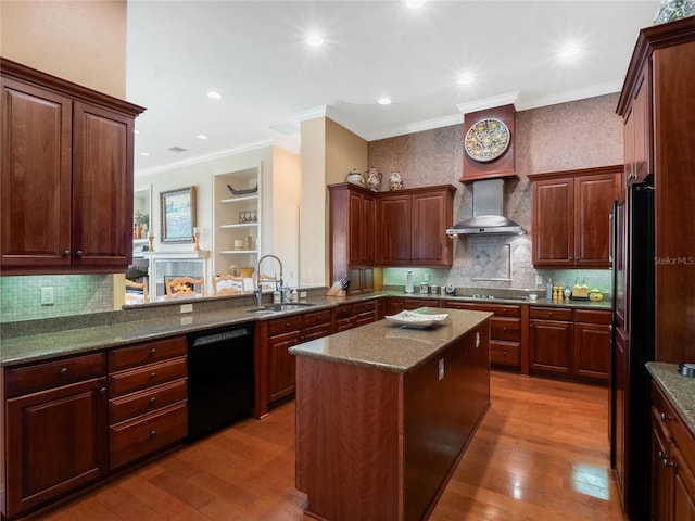 kitchen featuring wall chimney exhaust hood, a kitchen island, hardwood / wood-style floors, black appliances, and a sink