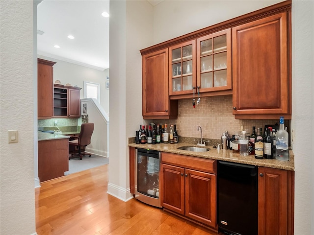 bar with light wood finished floors, decorative backsplash, a sink, wet bar, and beverage cooler