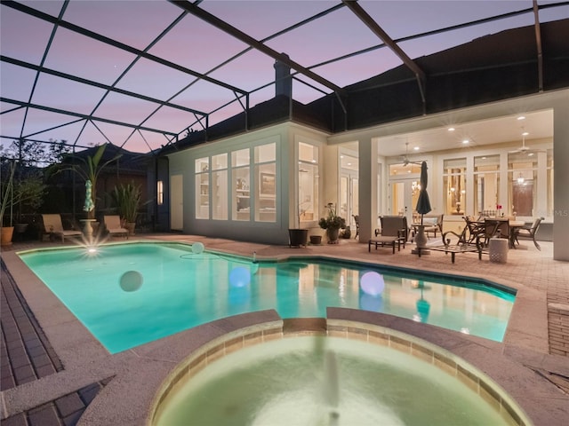 pool at dusk with a lanai, a patio area, and a pool with connected hot tub