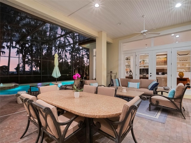 patio terrace at dusk featuring glass enclosure, ceiling fan, an outdoor hangout area, outdoor dining area, and a pool with connected hot tub