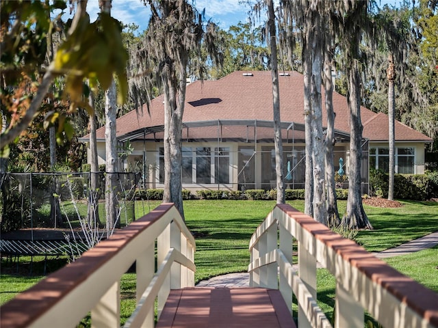 rear view of house featuring glass enclosure, a shingled roof, and a yard