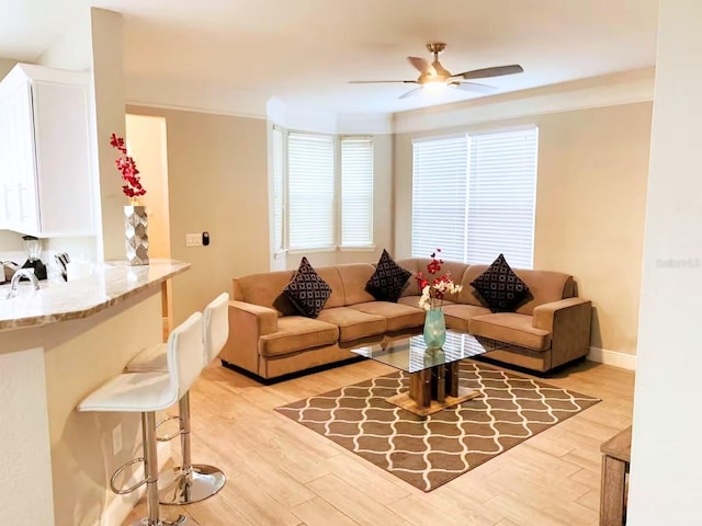 living area with light wood-style floors, crown molding, ceiling fan, and baseboards