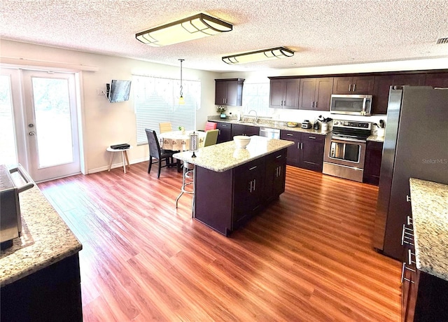 kitchen featuring a center island, appliances with stainless steel finishes, a sink, dark brown cabinetry, and wood finished floors