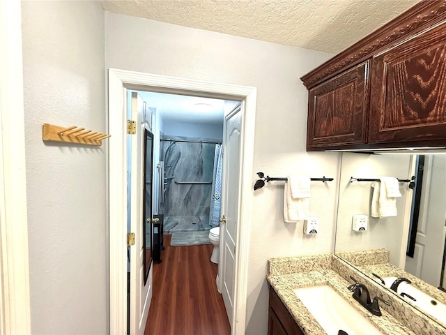 full bathroom with toilet, a shower with curtain, wood finished floors, a textured ceiling, and vanity