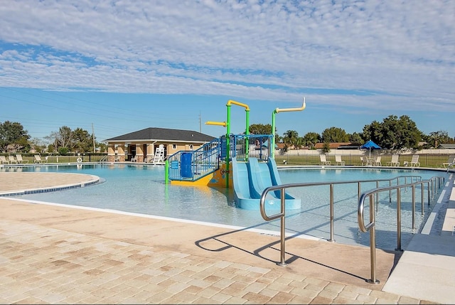 pool with a patio area, fence, and a water play area