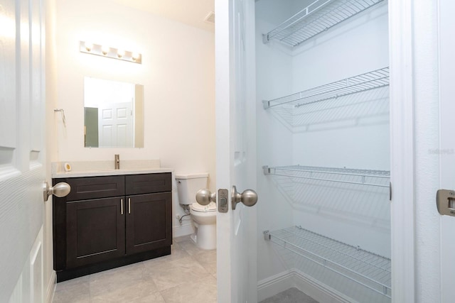 bathroom with baseboards, toilet, tile patterned floors, a spacious closet, and vanity