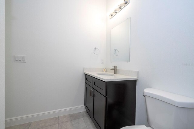 half bathroom with toilet, tile patterned flooring, baseboards, and vanity