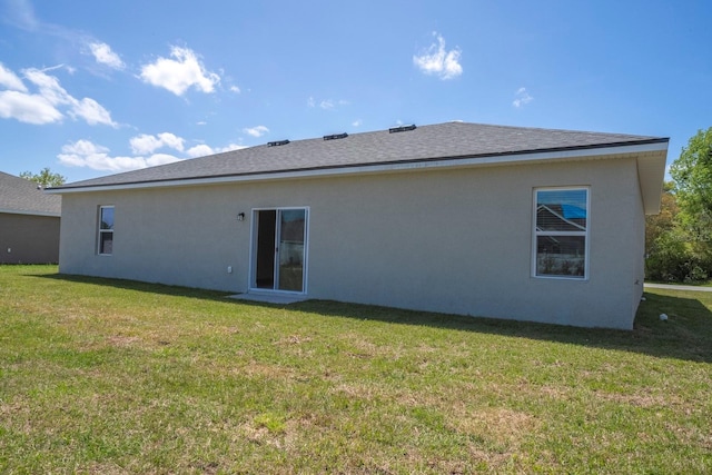 rear view of property with a yard, roof with shingles, and stucco siding